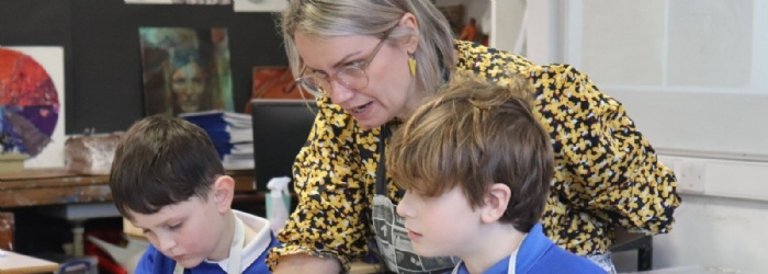 A Primary Pupil making a clay self-portrait at Sidmouth College with teacher helping 